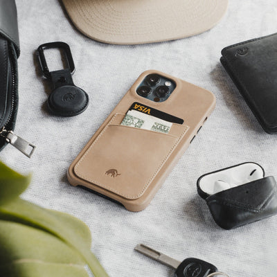 Tan minimalist phone wallet case holding a VISA card and cash, arranged with keys, AirPods, hat, and leather wallet.