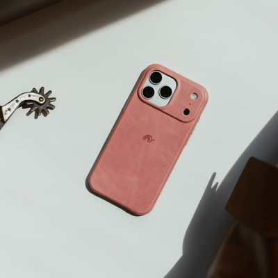Pink leather iPhone case with triple-camera cutout and small embossed elephant logo, lying on white surface with shadow.
