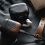 Two leather AirPods cases (black and brown), an AirPods Pro earbud, and a charging cable with bullstrap leather strap