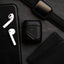 Black leather AirPods case next to AirPods, a phone, and a watch on a dark surface.