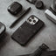 Black leather phone case with two card slots, styled with pen, earbuds case, camera and watch strap on textured surface.