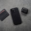 Black leather AirPods case next to a phone and wallet on a gray surface.